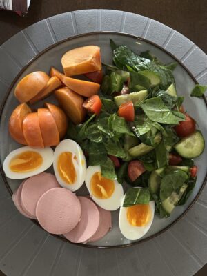 Healthy breakfast with spinach salad, cucumbers, tomatoes, soft-boiled eggs, turkey slices, and persimmon. Nutritious and quick recipe for a balanced morning meal.